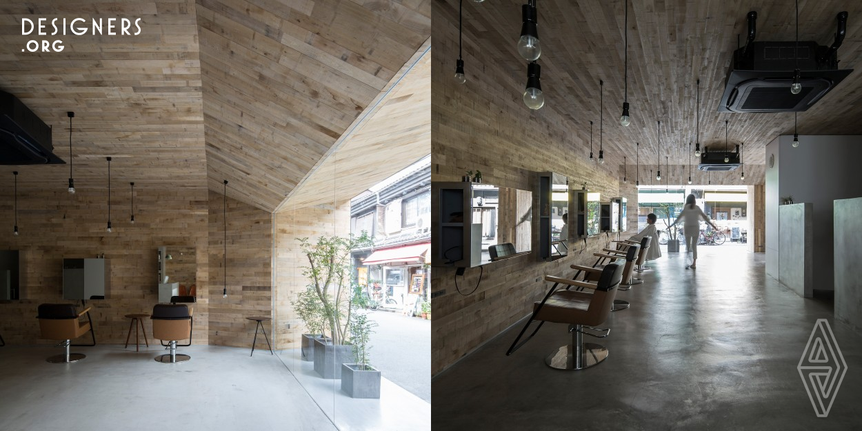 The interior of this salon is made up of uneven oak pieces in the middle of the sawing process. The unevenness of the oak absorbs the light from the outside, giving it depth and allowing it to penetrate deep into the room. The interior also extends outwards, giving the impression of a cave, with the interior and exterior designed as one. The glass facade reflects the activity of the salon in the city, making the movement of people part of the design.