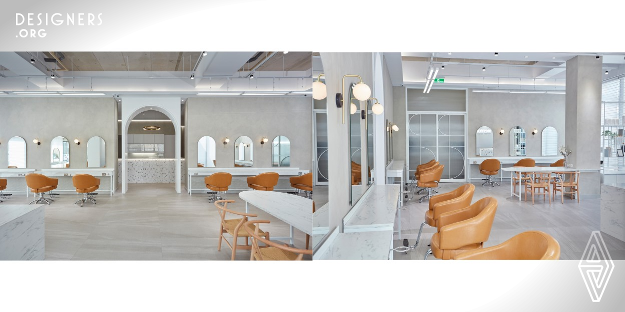 The salon is embedded in the center of the off-white wall with a soft glow from the downlight above. The irregular shapes of the metal ring pendant lights and the marbled countertop display a textured artistic atmosphere. People who step into the space are in pursuit of beauty. The modern atmosphere makes customers look forward to the next transformation. Through the white high archway, the light dims and deep gray tones linger.