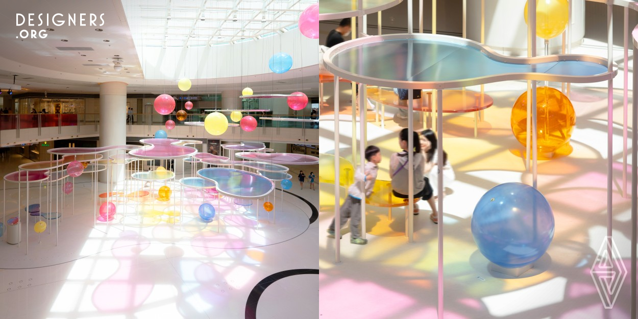 The pavilion is located in a landmark shopping mall in Hong Kong and aimed to celebrate the first summer after the pandemic by creating a colorful and vibrant atmosphere. The design incorporates layers of colorful acrylic panels that reflect sunlight and create shades of different colors on the ground. The strategic positioning of the panels creates an open and accessible space for the public to rest and play. Inspired by the dynamic nature of Hong Kong, the pavilion symbolizes hope, positivity, and the energy of the city. 