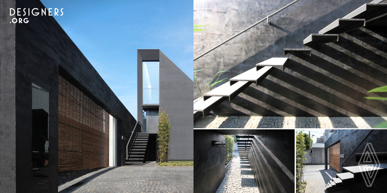 This sculptural black residence was planned in a quiet residential area of Tokyo. The site is narrow at the entrance and elongates towards the back, forming a slender shape. While complying with Japanese architectural regulations, such as shadow regulation on neighboring lands and building height restrictions, the design aims to create dynamic spaces that capitalize on this slender site shape. The approach features a monolithic black wall integrated with the architecture, making the exterior appearance striking, while the cantilevered stairs leading to the entrance enrich the sequence.