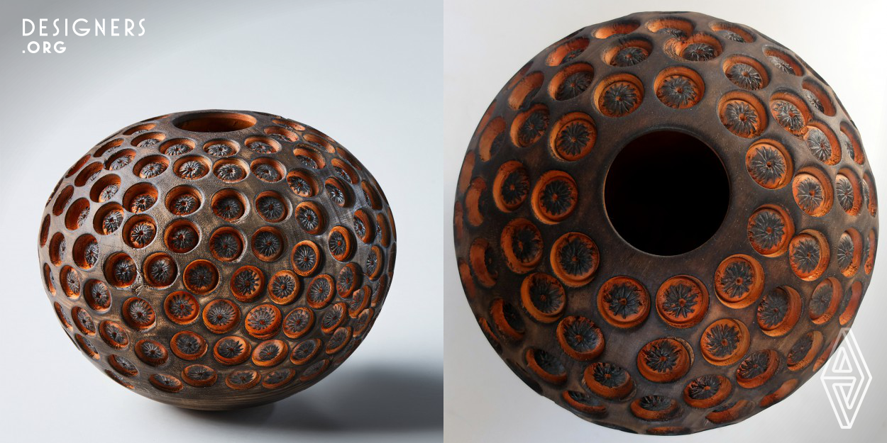 The concept of the design is based on the transformation of wood species that have no grain or color into an object vessel pleasing to the eye and additionally achieving an interesting haptic feeling. The design object is handcrafted, beginning with woodturning for forming the outside and hollowing the inside of the object. Drilling and forming the holes into the outer surface comes next, as well as adding color stain. The usage of a pyrographic pen brings further embellishment onto the piece. Finally the object is charred black, resulting in a soft and warm touch, as well as adding contrast.